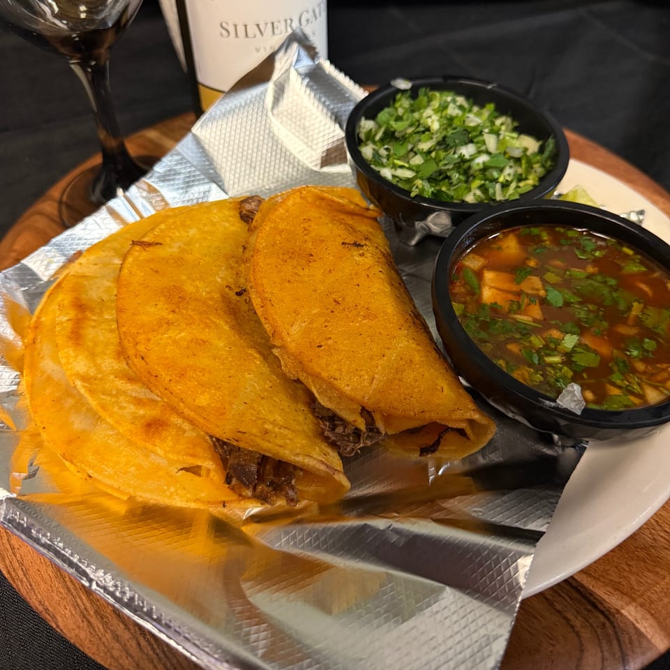 Three El Jarocho II birria tacos with consome and cilantro-onion relish on a foil-lined plate.