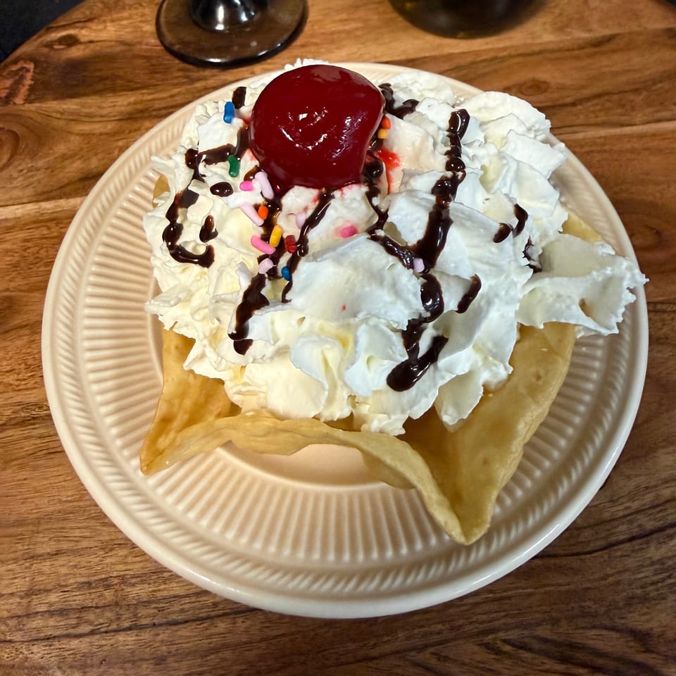 Fried ice cream dessert with whipped cream, chocolate syrup, sprinkles, and a cherry on top.
