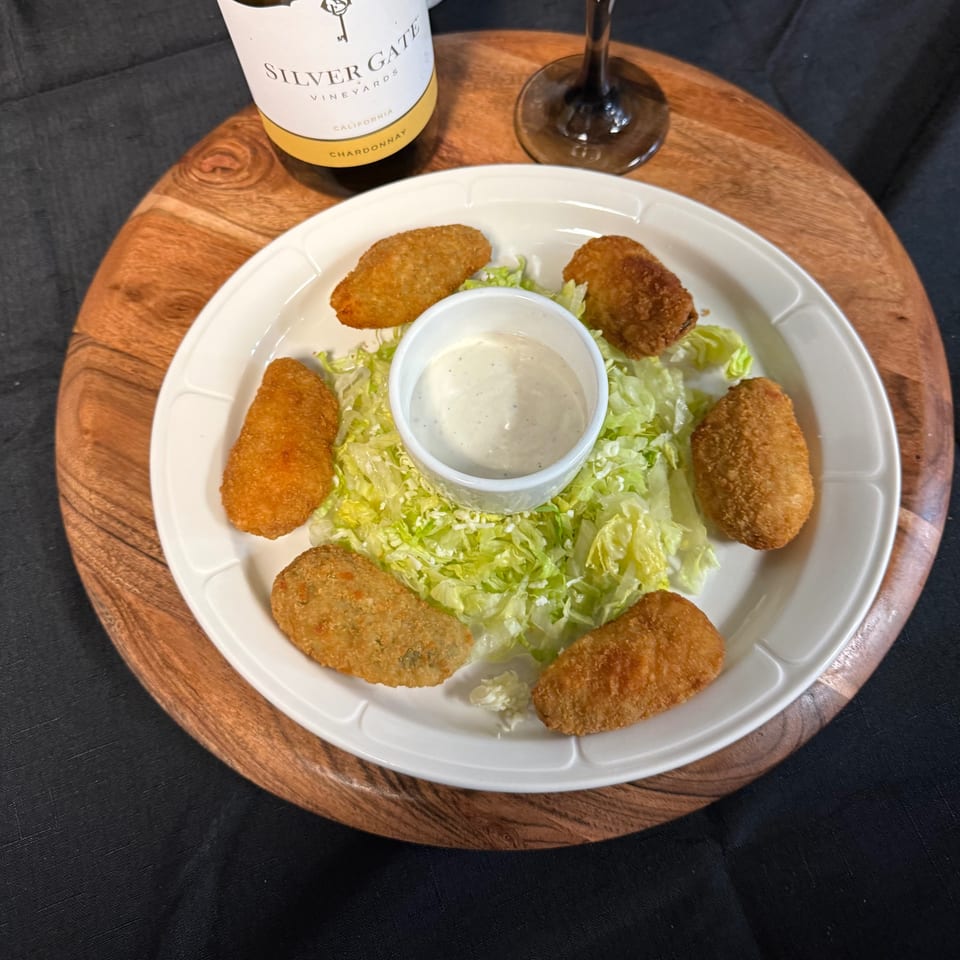Six golden-brown jalapeño poppers with a side of ranch dressing on a bed of shredded lettuce.