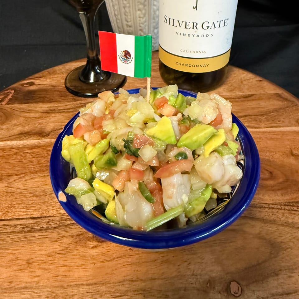 Mexican salad with avocado, tomato, and onion, topped with a small Mexican flag, next to a wine bottle.