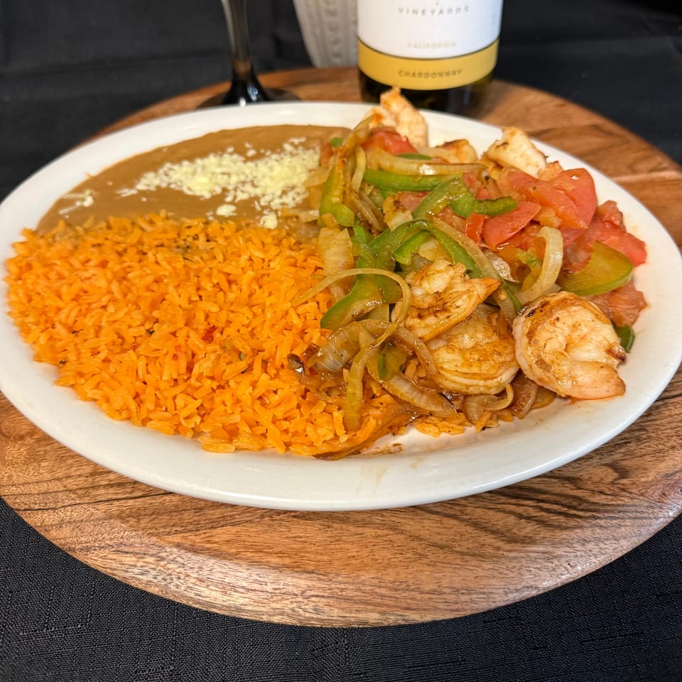 Shrimp fajitas with rice and refried beans, served on a white plate with a wine bottle.